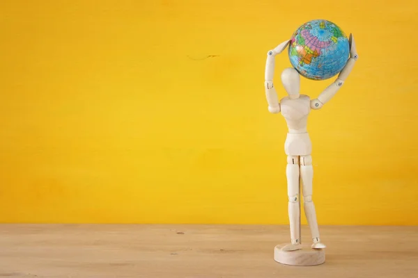 Houten dummy figuur bedrijf globe over gele achtergrond. ruimte voor tekst. — Stockfoto