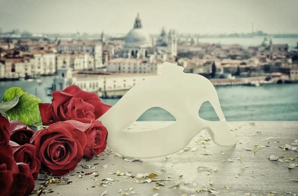 Imagem de elegante máscara veneziana e rosas vermelhas sobre mesa de madeira em frente ao fundo embaçado Veneza . — Fotografia de Stock