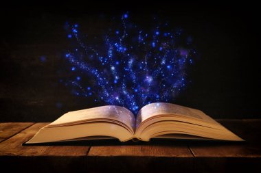 Tahta masanın üzerinde parıltılı kaplamalı açık antik kitap görüntüsü.