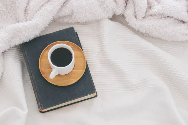 Tasse Kaffee auf dem alten Buch über kuscheliger weißer Decke. Ansicht von oben. — Stockfoto