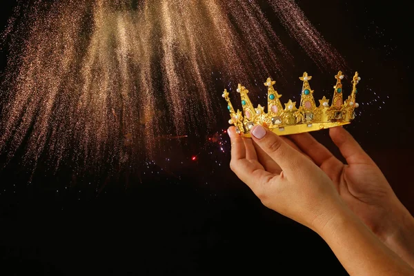 Mano della donna in possesso di una corona per la vittoria spettacolo o vincere il primo posto su sfondo nero con sovrapposizione glitter . — Foto Stock