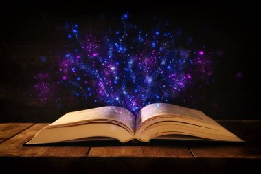 Tahta masanın üzerinde parıltılı kaplamalı açık antik kitap görüntüsü.