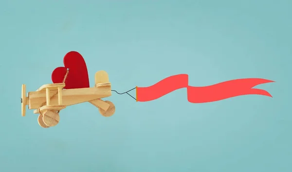 Aftelkalender voor Valentijnsdag achtergrond. Houten speelgoed-vliegtuig met hart en lint vliegen in de lucht. — Stockfoto