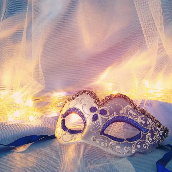 Image of delicate elegant venetian mask over blue silk and tulle