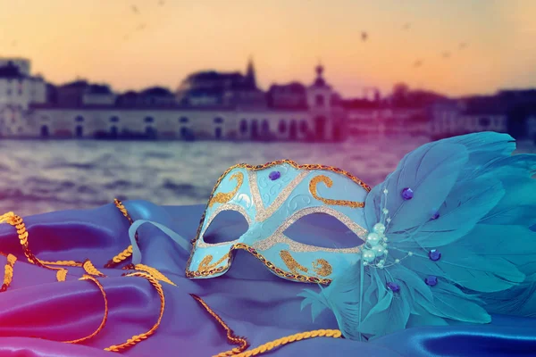 Image of elegant venetian mask on silk fabric in front of blurry Venice background.