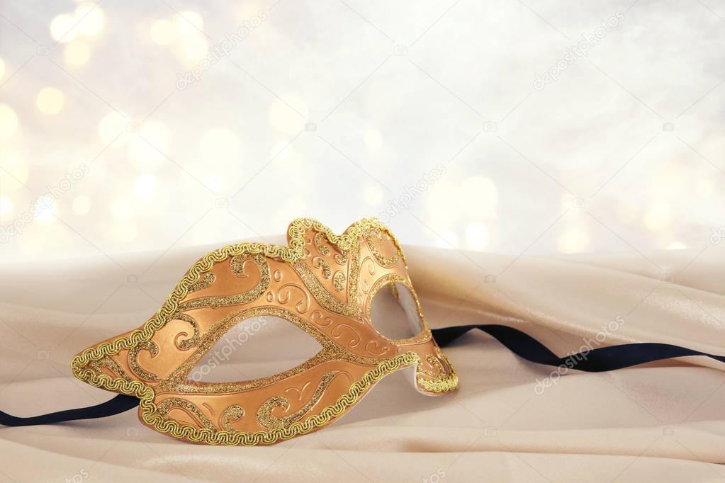 Image of elegant gold venetian mask over delicate silk fabric background.