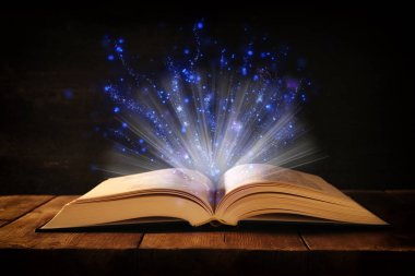 Tahta masanın üzerinde parıltılı kaplamalı açık antik kitap görüntüsü.
