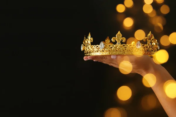 Mano de mujer sosteniendo una corona para mostrar victoria o ganando el primer lugar sobre fondo negro con superposición de brillo . — Foto de Stock