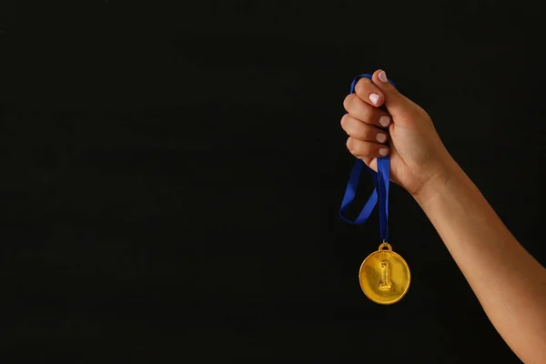 Woman hand holding gold medal against black background. Award and victory concept. — Stock Photo, Image