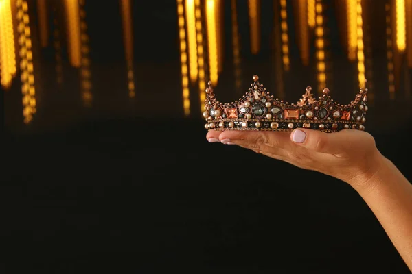 Mano della donna in possesso di una corona per la vittoria spettacolo o vincere il primo posto su sfondo nero con sovrapposizione glitter . — Foto Stock