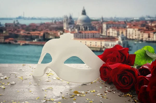 Image of elegant venetian mask and red roses over wooden table in front of blurry Venice background. — Stock Photo, Image