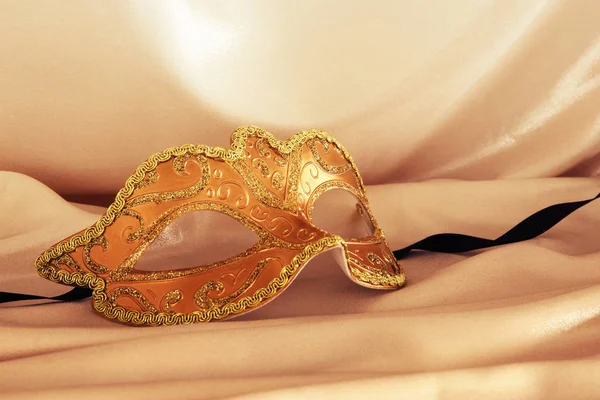 Image of elegant venetian mask over gold silk background.