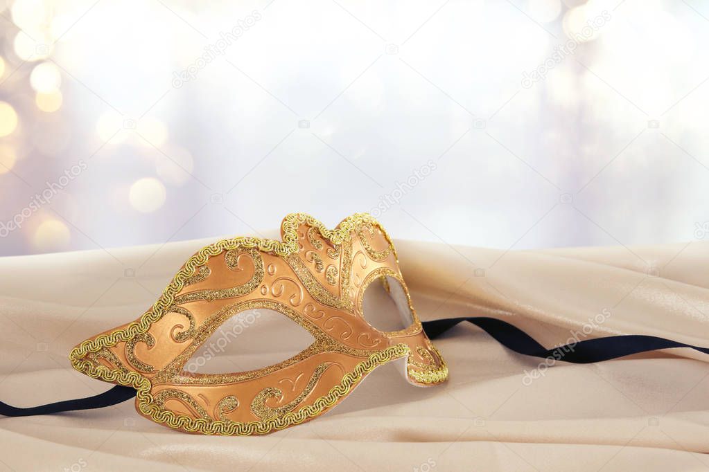 Image of elegant gold venetian mask over delicate silk fabric background.