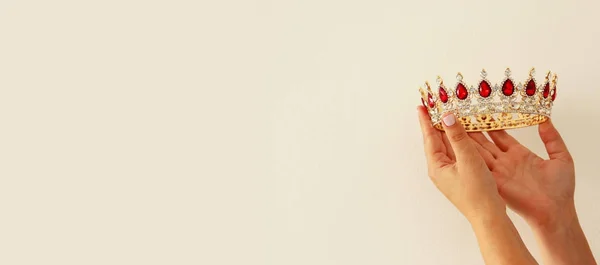 Woman\'s hand holding a crown for show victory or winning first place. White background. Copy space. Isolated.