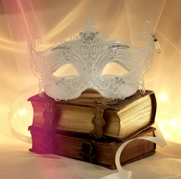 Image of delicate and elegant white venetian mask over vintage old books in front of tulle background. — Stock Photo, Image