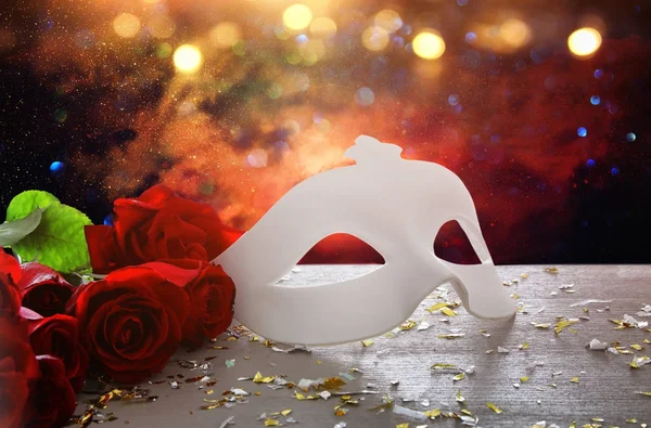 Bild einer eleganten venezianischen Maske und roter Rosen über einem Holztisch — Stockfoto