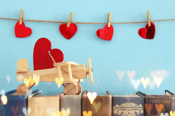 Valentine's day background. Wooden toy plane with heart over old books.