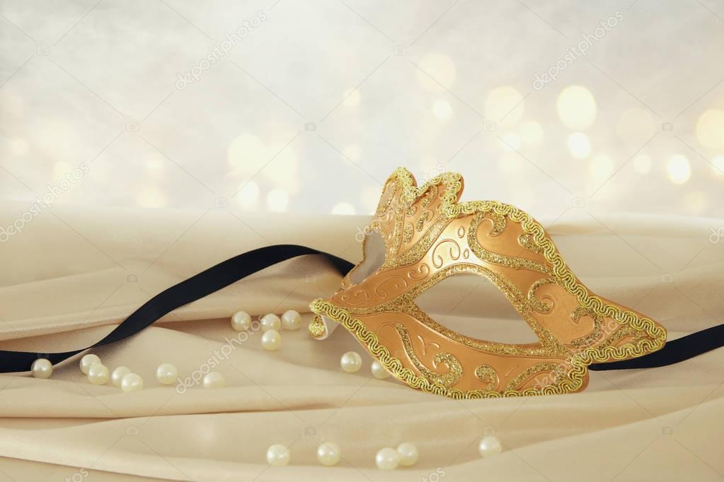 Image of elegant gold venetian mask over delicate silk fabric background.