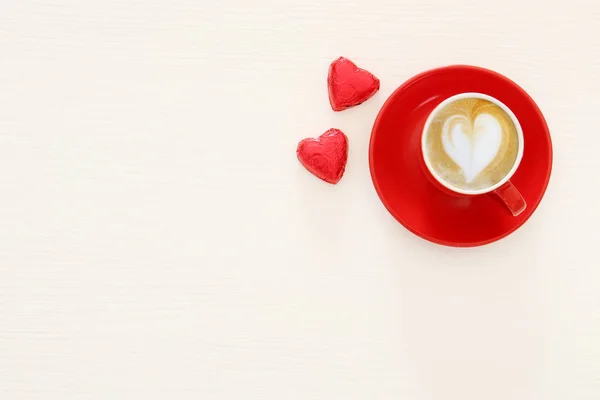 Tło valentine's day. czerwony kubek kawy z pianką kształt serca i czekolady. Widok z góry obrazu. — Zdjęcie stockowe