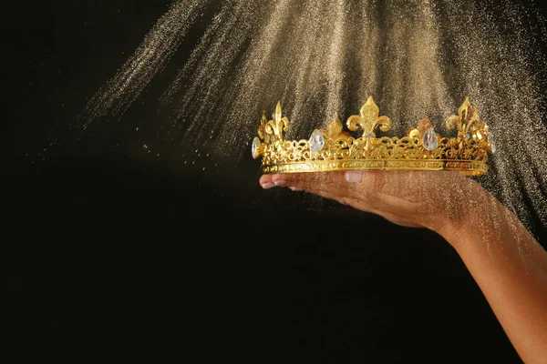 Mão de mulher segurando uma coroa para mostrar a vitória ou ganhar o primeiro lugar sobre o fundo preto com brilho sobreposição . — Fotografia de Stock