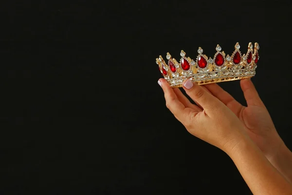 Main de femme tenant une couronne pour montrer la victoire ou gagner la première place sur fond noir . — Photo