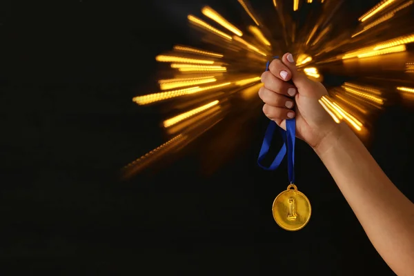 Frauenhand mit Goldmedaille vor schwarzem Hintergrund mit Glitzerüberzug. Auszeichnung und Siegerkonzept. — Stockfoto