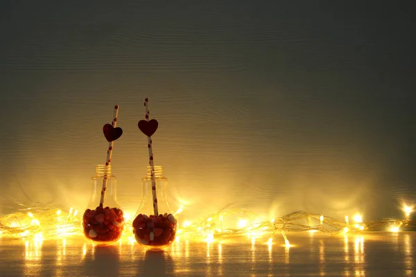 Aftelkalender voor Valentijnsdag romantische achtergrond met plastic lampje met hart vorm zoete snoepjes en feestelijke verlichting op tafel. — Stockfoto