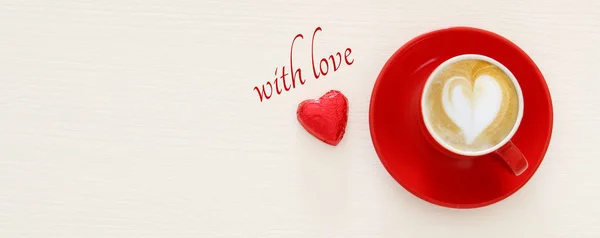 Fond de Saint-Valentin. tasse de café rouge avec mousse en forme de coeur et chocolat. Image vue du dessus . — Photo