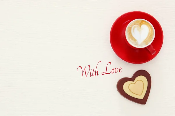 Fond de Saint-Valentin. tasse de café rouge avec mousse en forme de coeur et chocolat. Image vue du dessus . — Photo