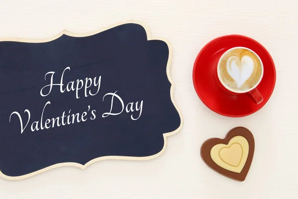 Der Hintergrund des Valentinstages. rote Tasse Kaffee mit herzförmigem Schaum und Schokolade. Bild von oben. — Stockfoto