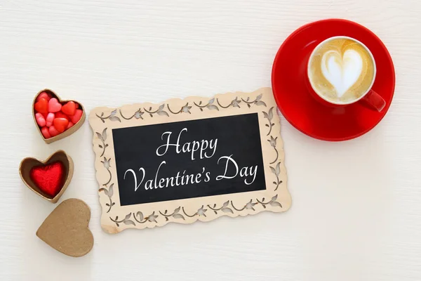 Der Hintergrund des Valentinstages. rote Tasse Kaffee mit herzförmigem Schaum und Schokolade. Bild von oben. — Stockfoto