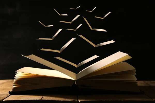 Bild eines offenen antiken Buches über einem Holztisch mit fliegenden Seiten. — Stockfoto