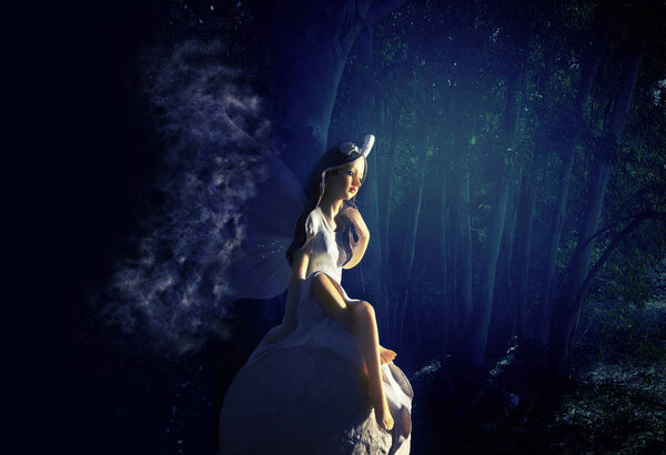 Image of magical little fairy in the forest sitting over the stone