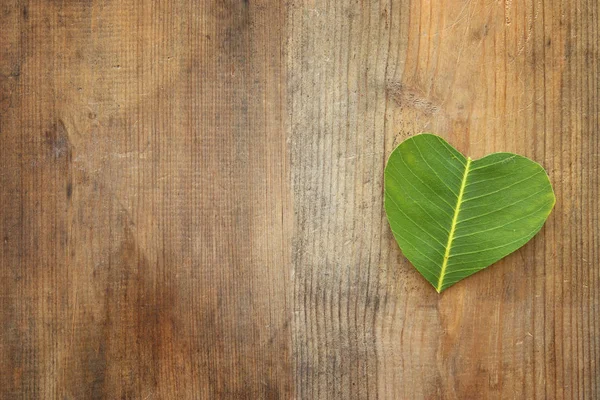 Foglia a forma di cuore sopra tavolo in legno. ecologia e salute . — Foto Stock