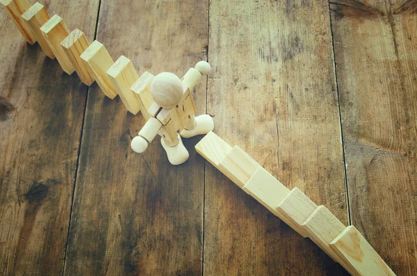 A wooden dummy stopping the domino effect. retro style image executive and risk control concept.
