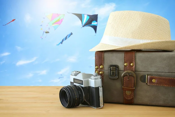 Reiziger vintage bagage, camera en fedora hoed over houten tafel infront van blauwe hemel en kleurrijke kite. vakantie en vakantie concept. — Stockfoto