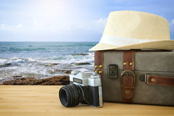 Reiziger vintage bagage, camera en fedora hoed over houten tafel infront van zee landschap. vakantie en vakantie concept. — Stockfoto