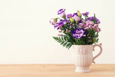 ahşap masa ve beyaz arka plan üzerinde vazoda mor çiçekler buket yaz.