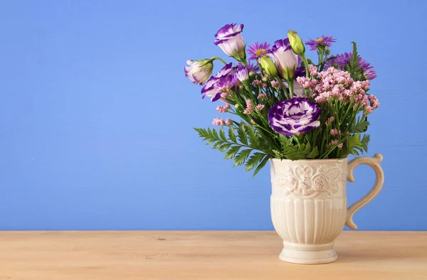 Ramo de flores de color púrpura en el jarrón sobre la mesa de madera y fondo azul . —  Fotos de Stock