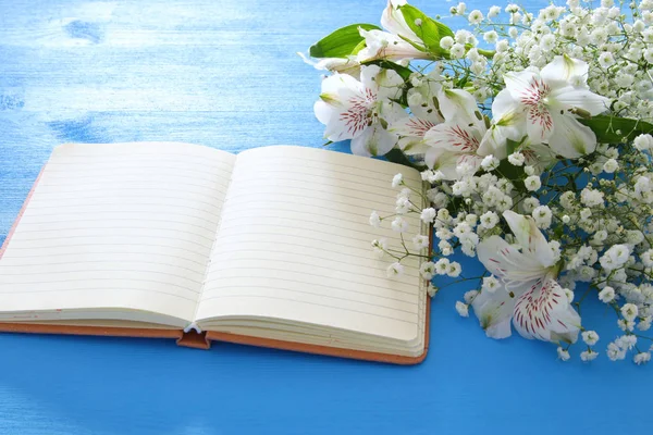 Κάτοψη του λευκά όμορφα άνθη διακανονισμού και κενό σημειωματάριο ανοιχτό μπλε φόντο ξύλινη. Χώρο αντίγραφο. — Φωτογραφία Αρχείου