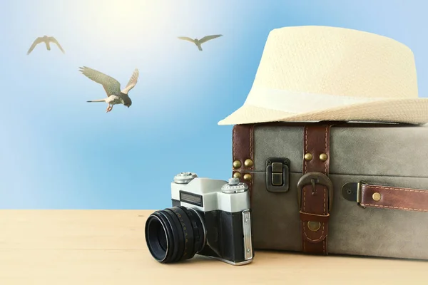 Reiziger vintage bagage, camera en fedora hoed over houten tafel infront van blauwe hemel en vogels. vakantie en vakantie concept. — Stockfoto