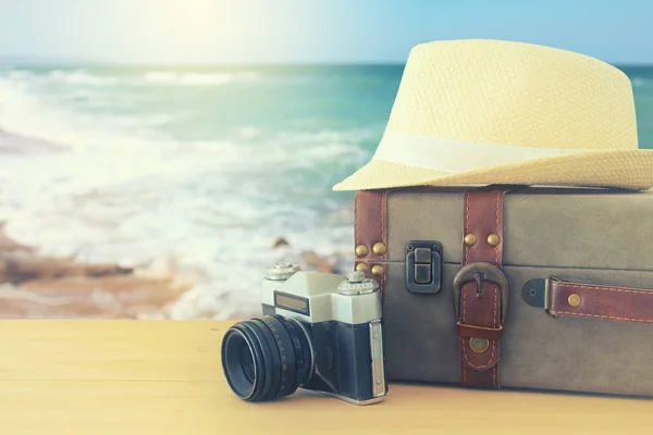 Reiziger vintage bagage, camera en fedora hoed over houten tafel infront van zee landschap. vakantie en vakantie concept. — Stockfoto