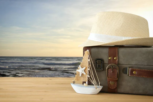 Traveler vintage luggage, boat and fedora hat over wooden table infront of sea landscape. holiday and vacation concept. — Stock Photo, Image