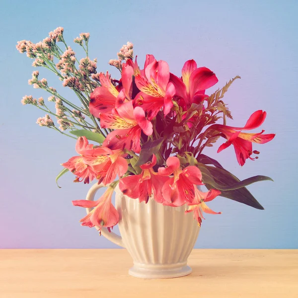 Sommerstrauß roter Blumen in der Vase über Holztisch und blauem Hintergrund. — Stockfoto