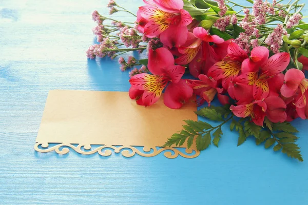 Top view of red beautiful flowers arrangement and empty letter over blue wooden background. Copy space. — Stock Photo, Image