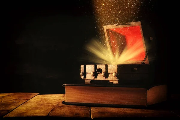 Imagen del misterioso cofre del tesoro con luz de purpurina y humo sobre un viejo libro sobre una mesa de madera . — Foto de Stock