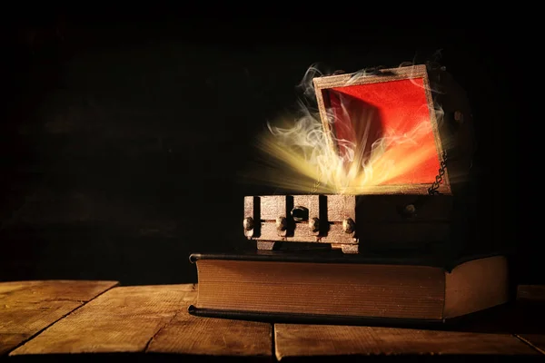 Bilden av mystiska skattkista med ljus och rök över gammal bok på träbord. — Stockfoto