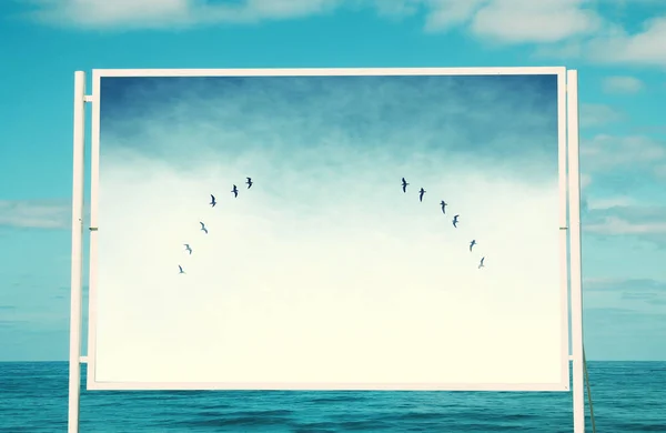 Image de panneau blanc sur la plage avec photo d'oiseaux volants au-dessus du ciel . — Photo