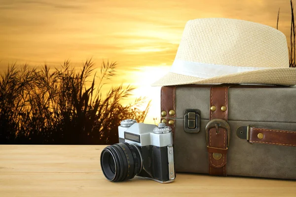 Equipaje vintage viajero, cámara y sombrero fedora sobre mesa de madera frente a un campo en la luz del atardecer. vacaciones y concepto de vacaciones . —  Fotos de Stock