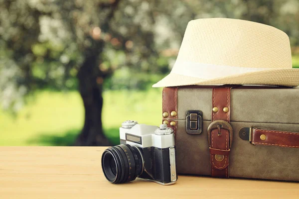 Reiziger vintage bagage, camera en fedora hoed over houten tafel infront van bokeh landschap. vakantie en vakantie concept. — Stockfoto